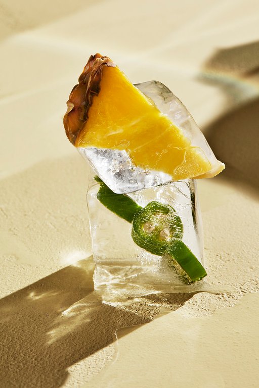 A stylized photo a pineapple slice and a jalapeño in an ice cube